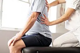 Therapist examining the lower back of a man sitting on the edge of a treatment couch