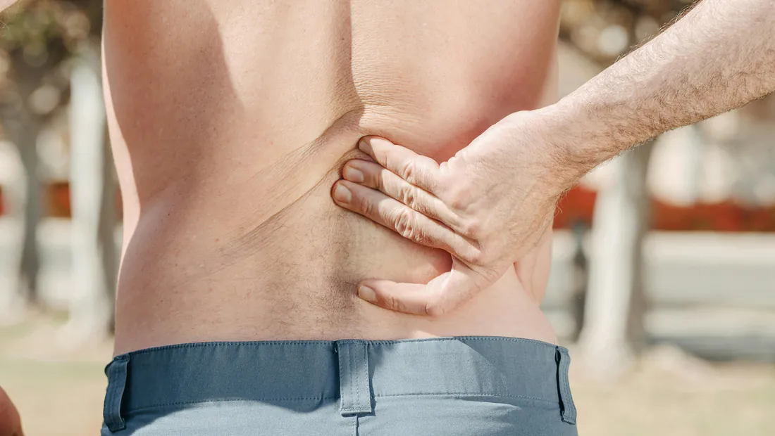 Close-up of a man pressing one hand into his aching lower back
