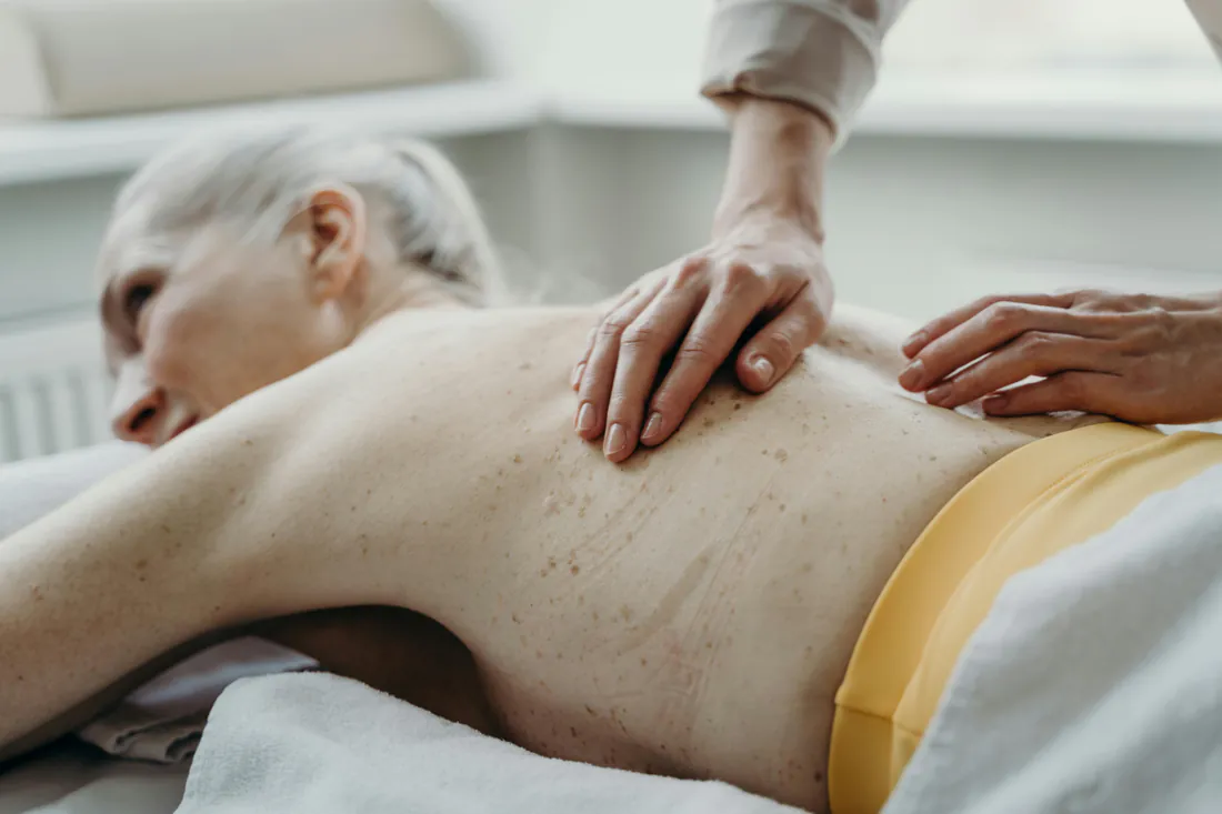 Therapist's hands treating the back of an older woman lying on a treatment couch