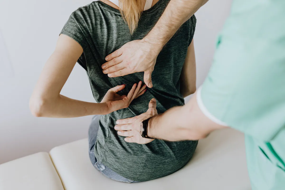 Clinician examining a woman's lower back as she points to a sudden, painful spot