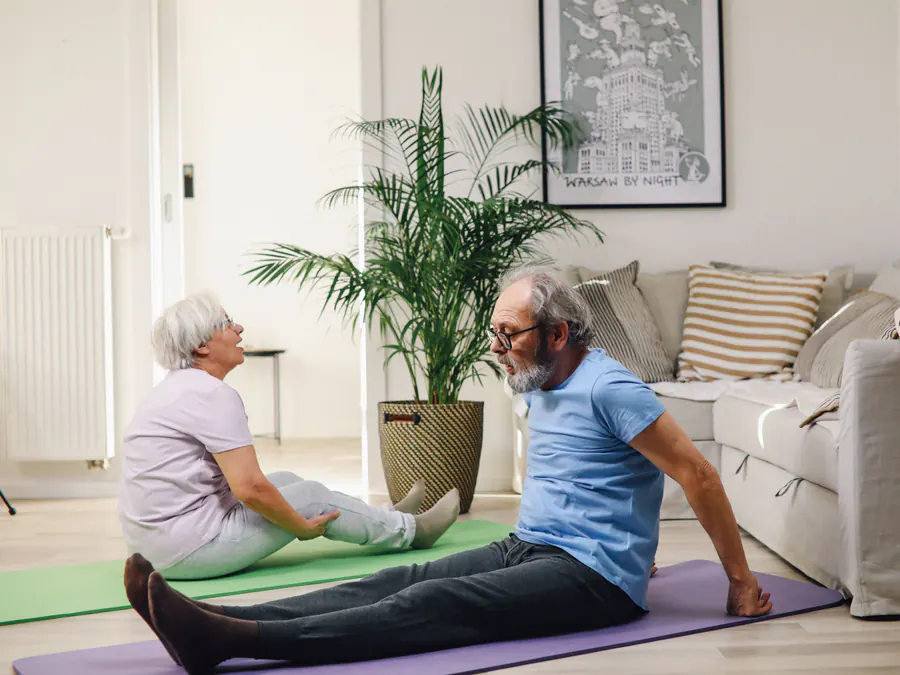 Older couple doing relaxed stretching exercises together on mats in their bright living room